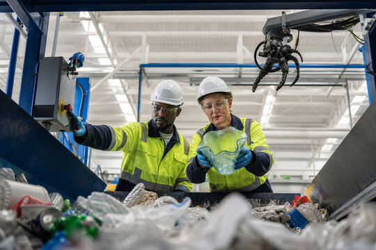 Two workers in safety gear inspect a sorting line in a bright industrial facility, overseeing waste processing. A focused moment highlighting teamwork and recycling.