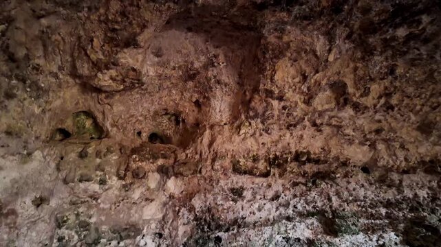 Rugged cave walls show ancient, textured earth tones. Streaks of moss and mineral deposits add depth. Natural lighting highlights rough, uneven surfaces. Ideal for archaeology, exploration