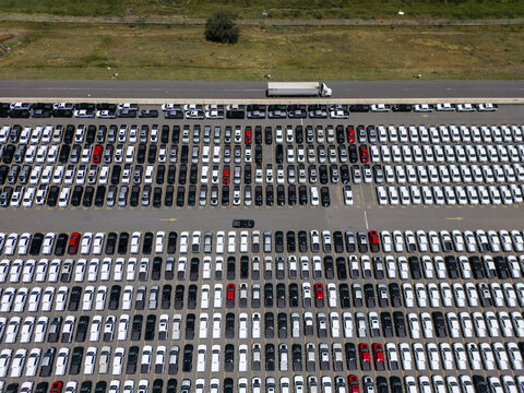 Aerial view of a car factory parking lot filled with rows of new vehicles, including trucks and cars, with a transport truck on the road in San Luis Potosi, San Luis Potosi, Mexico.