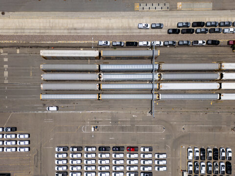 Aerial view of a car factory logistics hub with rows of new vehicles parked in a lot and freight trains loaded with cars for transport in San Luis Potosi, San Luis Potosi, Mexico.