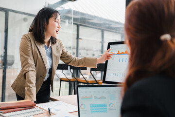 Asian Businesswoman Presenting Data Charts to Colleague on Computer Screen in Office