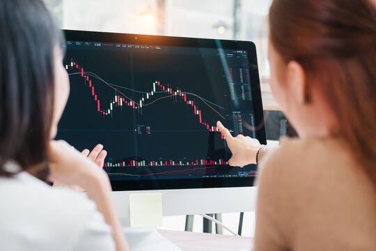 Two women analyzing stock market financial charts on computer screen in office
