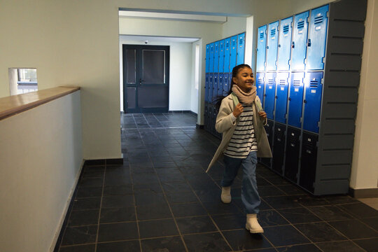 Teen African student walking through school corridor wearing pink scarf and backpack, copy space