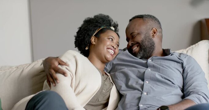 African American couple smiling then shifting into eye contact, leaning on sofa, seeking closeness