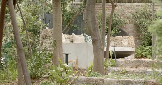 Camera is panning to reveal built-in stone seating nook with cushions in terraced garden