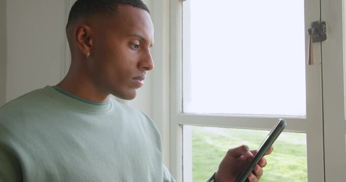 Phone lighting drawing African American man in green by window sipping mug scrolling phone laughing