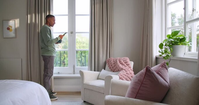 Checking phone, African American man in green shirt sipping mug reading by French doors, copy space