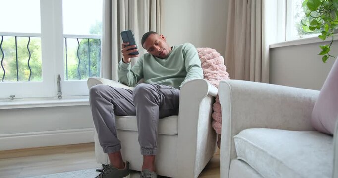 African American man sitting in armchair at home, checking phone, comparing card, confirming charge