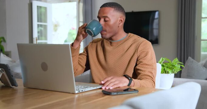African American man adjusting laptop typing at home table sipping mug for break glancing at noise