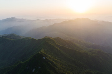 Fototapeta premium Layered mountain ranges at sunrise, with misty valleys and lush green slopes under warm morning light.