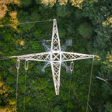 Aerial view of an electricity pylon surrounded by dense green forest with sunlight filtering through the trees in Poland.