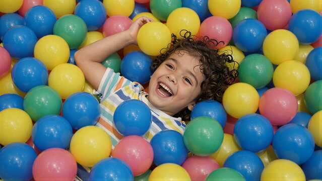 Child laughs joyfully buried in a colorful ball pit of bright plastic balls.