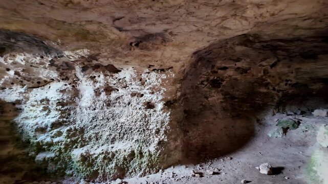 Cave walls glow with soft, natural light. Limestone textures show signs of age and moisture. Green moss clings to rocky surfaces. Ancient stone structures hint at hidden history
