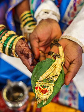 Traditional Maharashtrian Wedding Ritual bride and groom together holding a gold mangalsutra placed on a green betel leaf.