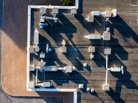 Aerial view of a flat roof featuring industrial HVAC ventilation systems, metal ducts, and pipes casting long shadows in the late afternoon sun, Cascais, Lisbon, Portugal.