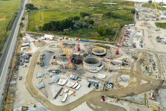 Aerial view of the American Fork wastewater treatment plant construction site with circular concrete vats, water tanks, cranes, and machinery in American Fork, Utah, United States.