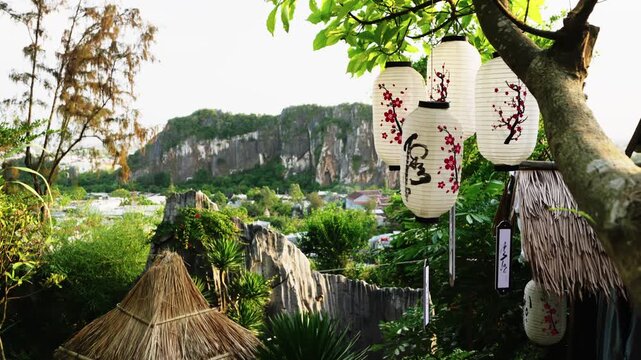 Landscape of hut in a forest and a tree with hanging paper lanterns on the mountains background. Travelling to Vietnam and enjoying exotic nature with hills and traditional culture decorations