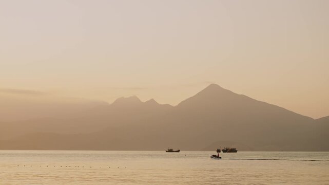 Breathtaking coastal landscape in Vietnam with rugged cliffs and distant mountains frame serene bay. Ocean stretches to the horizon and small boas sail leisurely while jet ski cuts across the waves