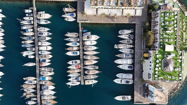 Aerial view of Mogan marina featuring rows of docked yachts and sailboats, turquoise water, and a building with a green rooftop terrace in Las Palmas, Canary Islands, Spain.