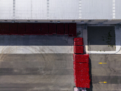 Aerial view of a logistic center with stacks of red crates on asphalt, yellow directional arrows, and a large industrial building roof in Santiago de Queretaro, Queretaro, Mexico.
