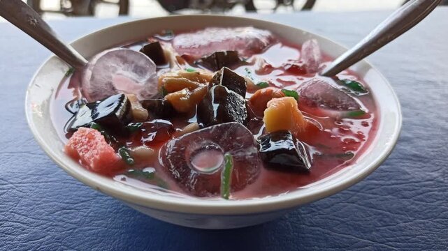 refreshing serving of classic Indonesian es campur, featuring shaved ice, colorful sweet ingredients, syrup, and condensed milk served in a traditional glass or bowl. This popular dessert showcases In