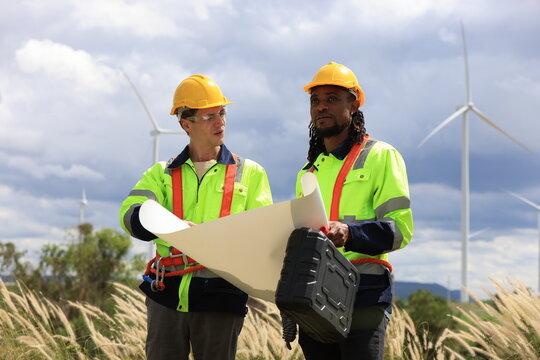 African american and caucasian engineers use laptop checking or maintenance wind turbines at windmill field farm. workers working at wind turbines farm. Alternative eco energy, environmental friendly