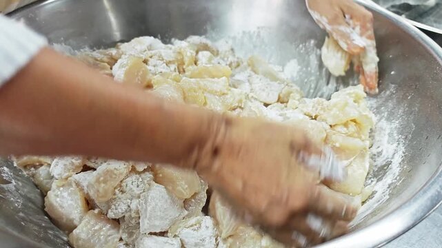 Chef hands mixing raw fish pieces with flour in a bowl.