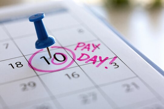 Close-up of a monthly calendar page showing the tenth day circled in pink marker with handwritten text pay day next to it and a blue pushpin marking the date