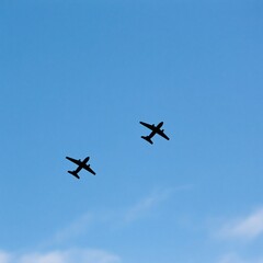 Fototapeta premium Two airplane silhouettes fly in formation against a clear blue sky with faint clouds below.