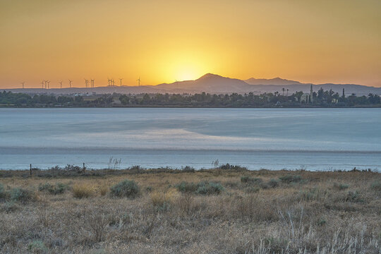Aerial view of Larnaca Salt Lake at sunset with wind turbines on the horizon and dry vegetation in the foreground in Cyprus, Cyprus.