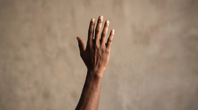 Raised hand symbolizing cultural diversity and unity against neutral background with depicts dark skinned hand raised high against textured beige background