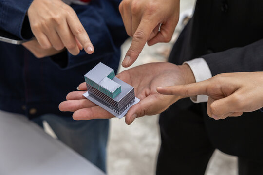 Business hand model architecture teamwork planning pointing miniature building project discussion around small architectural model palm showing collaborative design review and focused decision