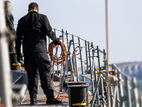 A man stands on a ship deck hold rope for resque man over board.