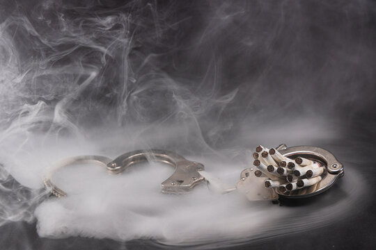 handcuffs with a cigarette on black background and smoke. Concept of addiction.	