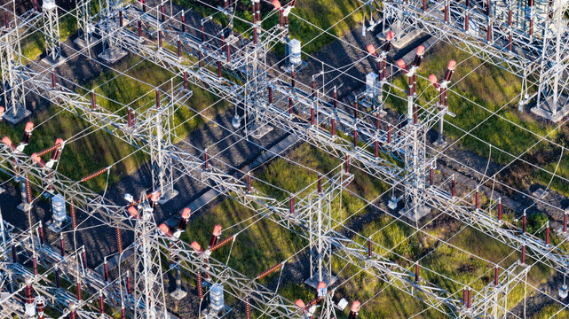 Aerial view of an electrical substation with metal towers, insulators, and power lines set against green grass in Reykjavik, Reykjavikurborg, Iceland.