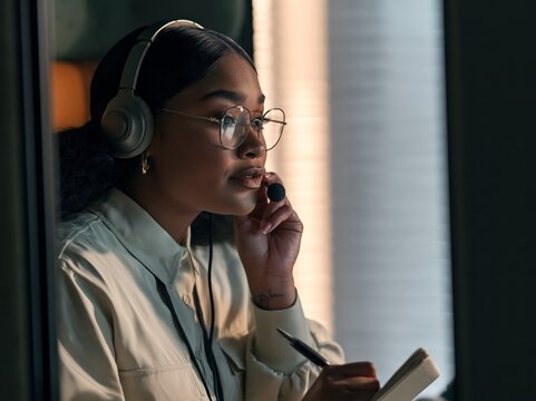 Medical interpreter takes notes during a video call in a remote work booth with headset and soft window light