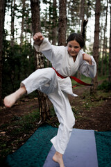 Young girl practicing a karate kick outdoors in a forest training session wearing a red belt and white gi © Nikola Spasenoski