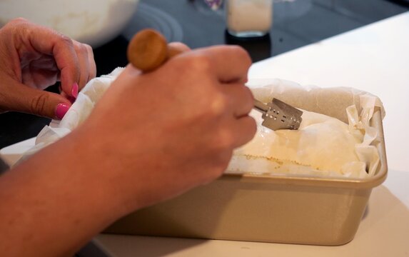 Woman scoring raw dough, taking a baked sourdough sandwich loaf out of oven, and rubbing butter over hot crust during homemade bread baking process