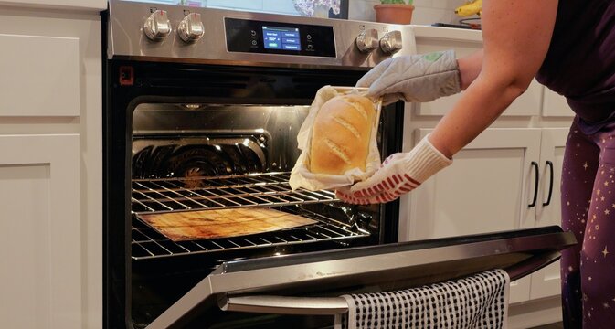 Woman scoring raw dough, taking a baked sourdough sandwich loaf out of oven, and rubbing butter over hot crust during homemade bread baking process