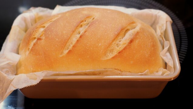 Woman scoring raw dough, taking a baked sourdough sandwich loaf out of oven, and rubbing butter over hot crust during homemade bread baking process