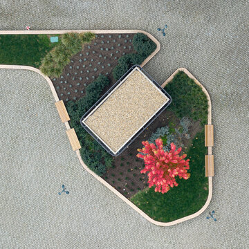 Aerial view of a small urban park featuring a rectangular structure, a vibrant red tree, and wooden benches surrounded by paved ground in Belgrade, Serbia.