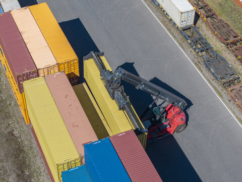 Aerial view of a reach stacker lifting a yellow shipping container at the Polzug Intermodal terminal with colorful containers and railway wagons in Dabrowa Gornicza, Poland.
