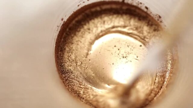 The process of mixing a golden-colored mixture or liquid with a metallic shimmering glitter effect in a container. 