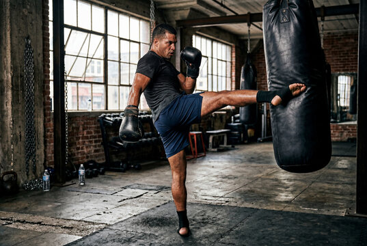 Male boxer performing a high kick on a heavy punching bag in a dark gym