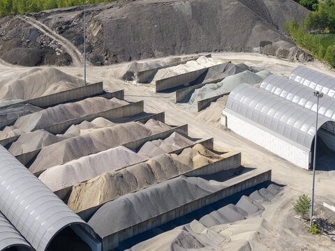 Aerial view of Masfalt Sp. z o.o. WMB aggregate storage facility with piles of gravel, sand, and crushed stone in concrete bins and industrial sheds in Dabrowa Gornicza, Poland.