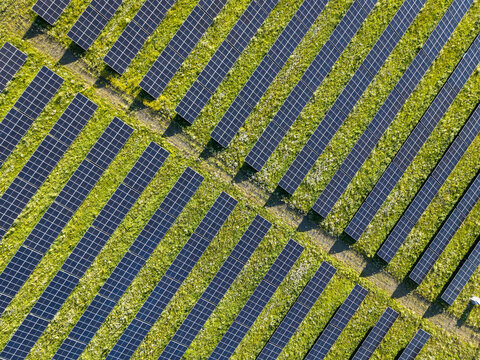 Aerial view of a large solar farm with rows of photovoltaic panels arranged in diagonal lines over a green grassy field in Poland.
