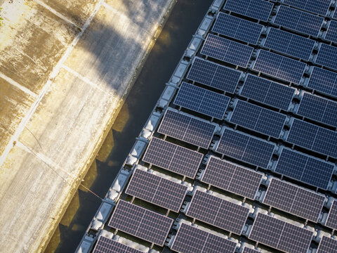 Aerial view of floating solar panels arranged in a grid pattern on the water surface next to a concrete embankment in Poland.