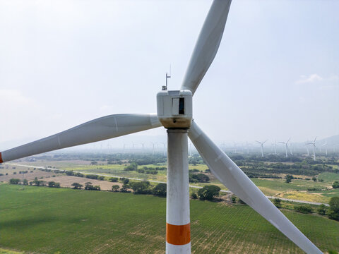 Aerial view of a wind turbine in a large wind farm with green fields and distant hills under a clear sky in La Ventosa, Oaxaca, Mexico.