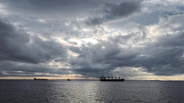 Panoramic overcast seascape with soft crepuscular rays breaking through dense clouds over commercial shipping lane