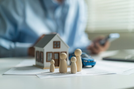 Close-up of wooden family dolls with house model and toy car on insurance policy document at desk.